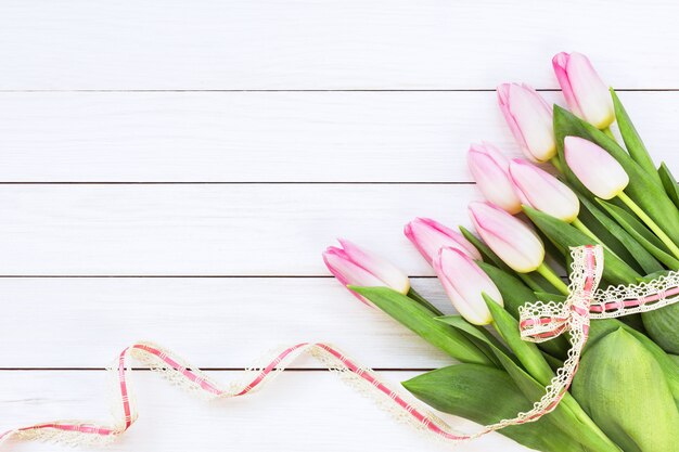 Buquê de tulipas cor de rosa decorada com fita em fundo branco de madeira.