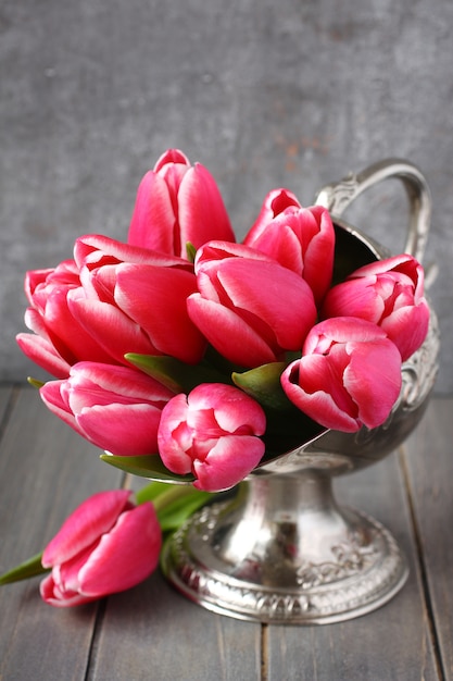 Buquê de tulipas cor de rosa em um vaso de metal no fundo de madeira