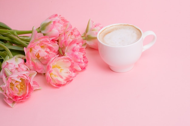 Buquê de tulipas cor de rosa, uma xícara de café em um fundo rosa