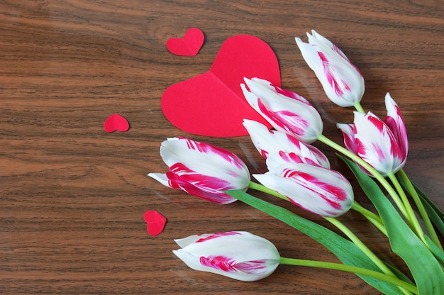 Buquê de tulipas e corações de papel vermelho em fundo de madeira