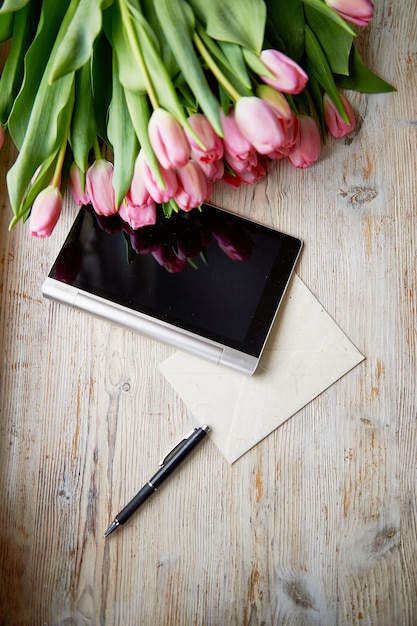 Buquê de tulipas em uma superfície de madeira perto do tablet caneta e papel