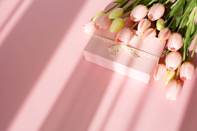 Buquê de tulipas tenras e caixa de presente isolada em um fundo rosa com sombra. Flores da primavera. Cartão de aniversário, mulher, dia das mães, casamento, dia dos namorados. Postura plana. Copie o espaço