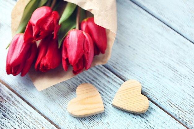 Buquê de tulipas vermelhas em um saco de papel com uma caixa de presente em uma mesa azul clara