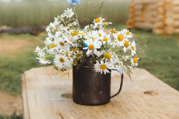 Buquê de verão de margaridas brancas, em um vaso de ferro, sobre um fundo de madeira, flores silvestres