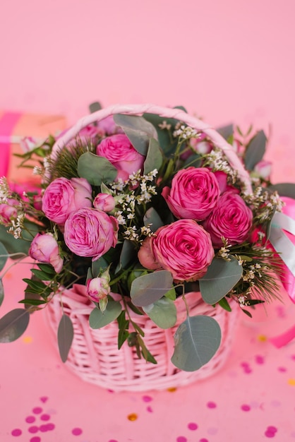 Foto buquê romântico de rosas e eucalipto em uma cesta em um fundo rosa com confete presente de aniversário dia da mulher dia da mãe dia dos namorados