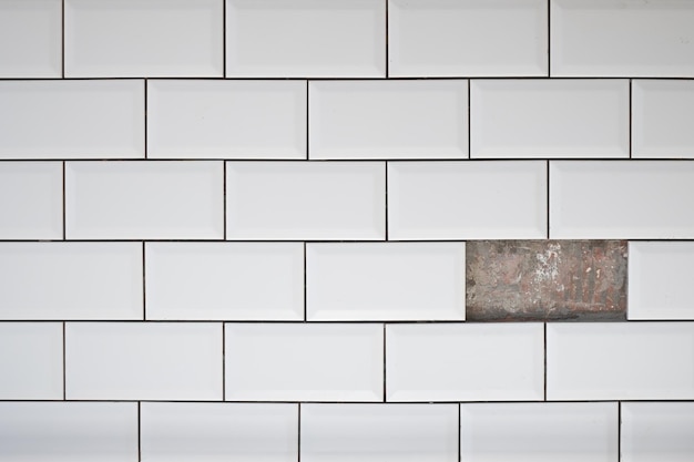 Buraco no azulejo branco cerâmico na parede da cozinha Um azulejo perdido na parede