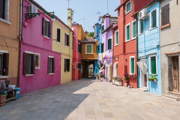 Burano, Venecia, Italia - 02 de julio de 2018: Vista panorámica de casas de colores brillantes de Burano es una isla en la Laguna de Venecia. La gente camina y descansa en las calles. Día soleado de verano y cielo azul.