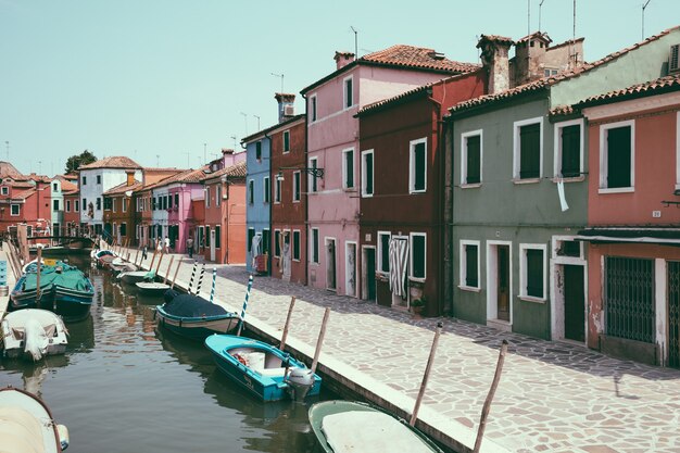 Burano, Venecia, Italia - 02 de julio de 2018: Vista panorámica de casas de colores brillantes y canal de agua con barcos en Burano, es una isla en la Laguna de Venecia. La gente camina y descansa en las calles.