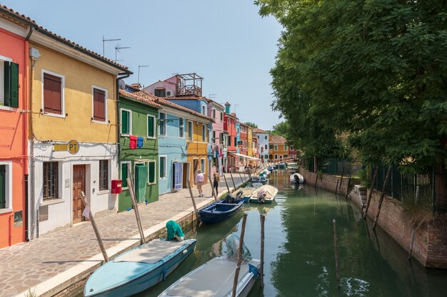 Burano, Venecia, Italia - 02 de julio de 2018: Vista panorámica de casas de colores brillantes y canal de agua con barcos en Burano, es una isla en la Laguna de Venecia. La gente camina y descansa en las calles.