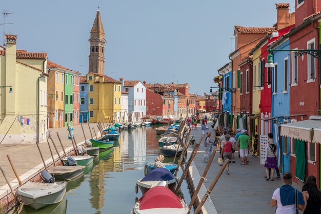 Burano, Venedig, Italien - 2. Juli 2018: Panoramablick auf bunte Häuser und Wasserkanal mit Booten in Burano, es ist eine Insel in der Lagune von Venedig. Menschen gehen und ruhen sich auf den Straßen aus