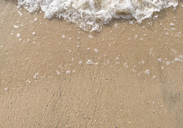 Foto burbuja blanca de ola de mar en la arena fina en la playa