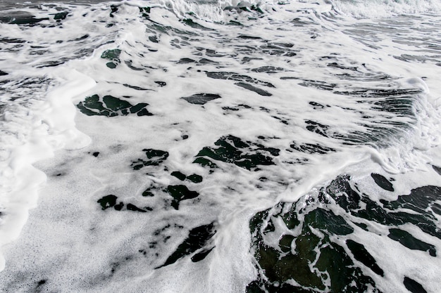 Burbujas blancas de olas rompen la playa de arena