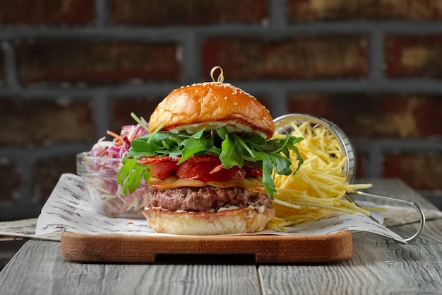 Burger auf dem Holztisch mit Käse, Speck, Tomaten, grünem und rotem Salat und Pommes Frites