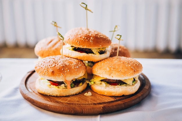 Burger auf einem runden Holzbrett. Brötchen mit Sesam. Haufen Burger auf einem weißen