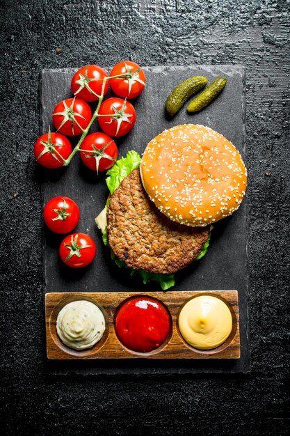 Burger auf einem Steinbrett mit Saucen und Tomaten auf einem Zweig