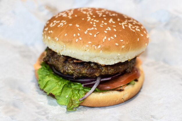 Burger auf Packpapierhintergrund. Schnitzel, Käse, Gemüse und Sesambrötchen. Straßen-Fastfood