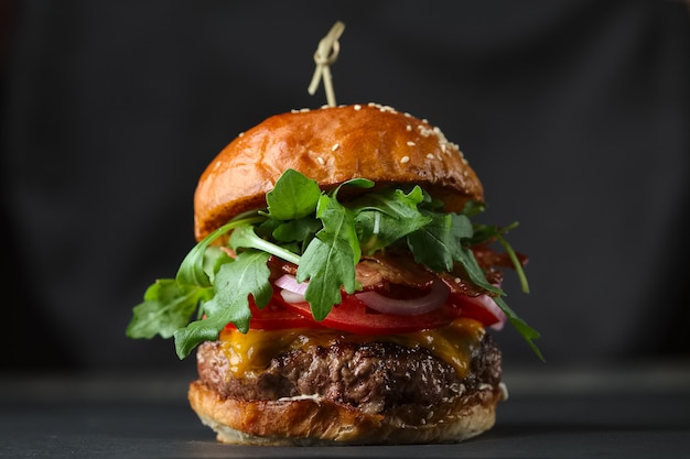 Burger auf schwarzer Oberfläche mit Käse, Speck, Tomaten, grünem Salat und Zwiebeln