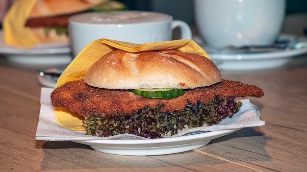 Burger com salada fresca, queijo e carne e uma chávena de café numa mesa de madeira.