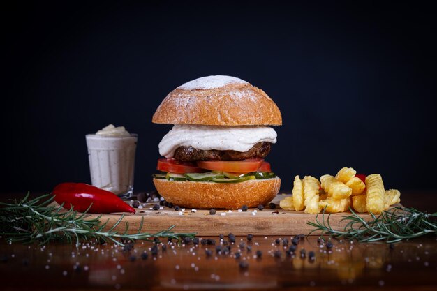 Foto burger de carne com queijo de tomate, pepino e molho servido em uma tábua de madeira preta burger de carne artesanal com batatas fritas feito à mão