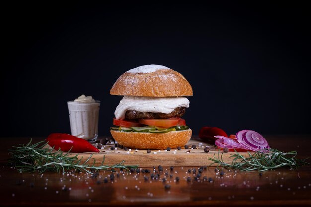 Foto burger de carne com queijo de tomate, pepino e molho servido em uma tábua de madeira preta. burger de carne artesanal feito à mão.