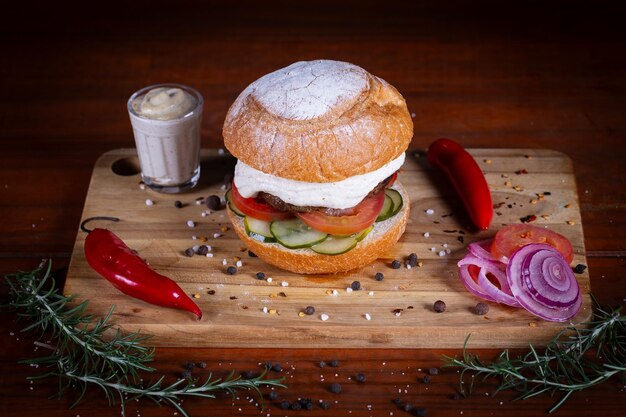 Foto burger de carne com queijo de tomate, pepino e molho servido em uma tábua de madeira preta. burger de carne artesanal feito à mão.