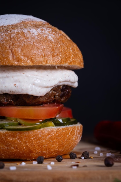 Foto burger de carne com queijo de tomate, pepino e molho servido em uma tábua de madeira preta. burger de carne artesanal feito à mão.