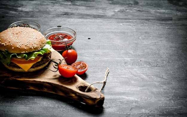 Burger mit den Zutaten und der Sauce auf dem Brett. Auf einer schwarzen Tafel.