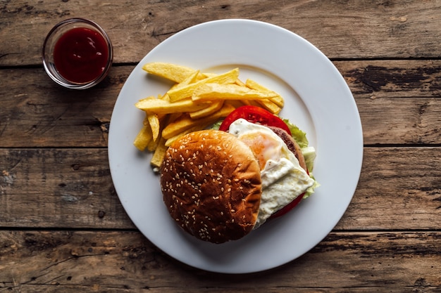 Burger mit Ei und Kartoffeln auf rustikalem Holztisch