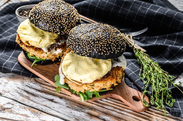 Burger mit einer schwarzen Brioche, Rührei, Rindfleischpastetchen und Rucola. Weißer Hintergrund. Draufsicht.