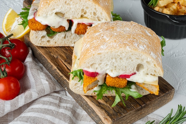 Burger mit Fischstäbchen frische Salattomate und Tartarsauce auf Holzschneidebrett gesetzt