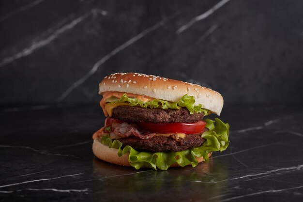 Burger mit Fleisch und Käse auf dem Tisch, amerikanische Küche, Nahaufnahme, Tomate, dunkler Hintergrund, Marmor,