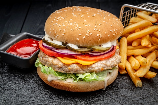 Burger mit Hühnerschnitzel und Pommes Frites auf dunklem Hintergrund