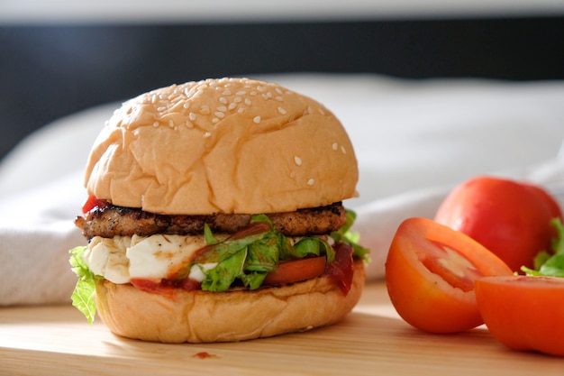 Burger mit Käse, Salaten und Gemüse auf einem weißen Holzbrett.