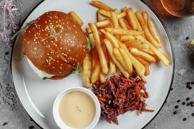 Burger mit Pommes und Sauce auf einem weißen Teller