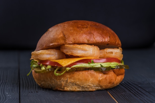 Burger mit Riesengarnelen, Käse, Salat und Tomate auf schwarzem Holzhintergrund.