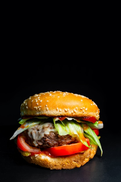 Burger mit Rindfleisch, Käse und Salat auf einem schwarzen Hintergrund