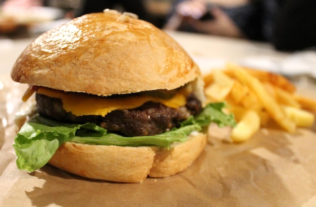 Burger mit Schweine- und Rinderkotelett, Käse und Salat mit Pommes Frites im Hintergrund, Fast Food