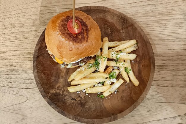 Burger mit Stock und Bratkartoffeln in einem Holzteller auf dem Tisch servieren