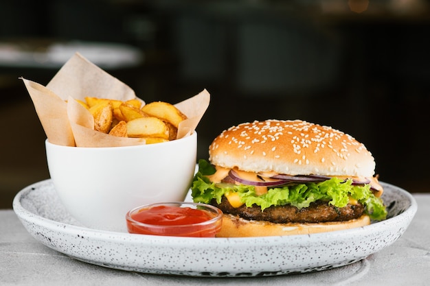 Burger-Nahaufnahme mit Salat und Sauce auf Betontisch, Restauranthintergrund. Big Burger mit Pommes und Ketchup.