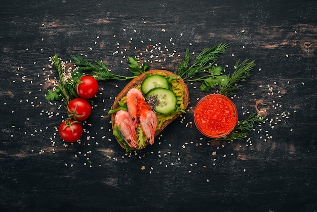 Burger, Sandwich mit Garnelen, Avocado, Kaviar und Gurke. Auf einem hölzernen Hintergrund. Ansicht von oben. Platz kopieren.