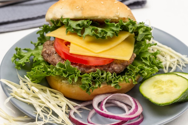 Burgerbrötchen auf Salatblatt mit Käse und Tomaten, gehackte Gurken und Zwiebeln auf grauem Teller