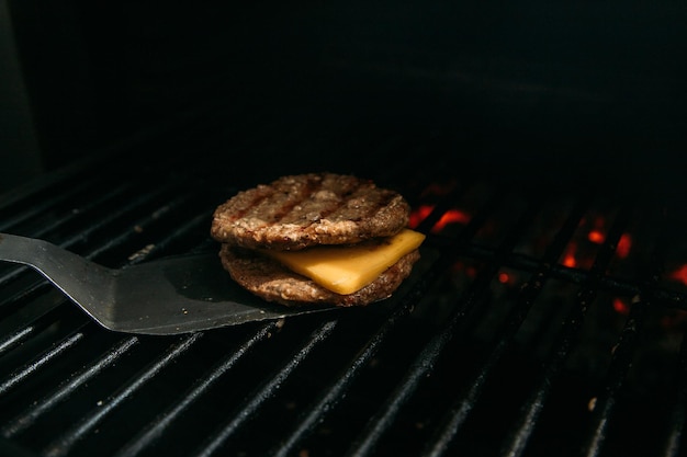 Burgerfleischzubereitung mit Käse auf dem schwarzen Hintergrund des Grills