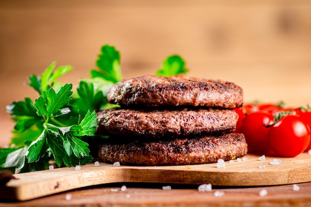 Burgergrill auf einem Schneidebrett mit Gemüse und Tomaten