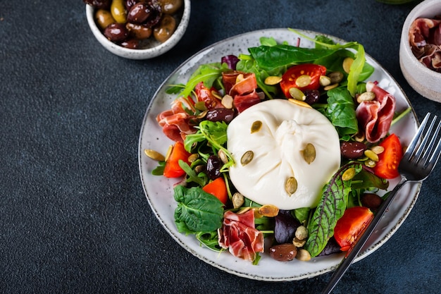 Burrata, italienischer Frischkäse aus Sahne und Milch von Büffeln oder Kühen. Burrata-Salat mit Tomaten und Salatmischung. Konzept der gesunden Ernährung. Keto-Diät-Salat.