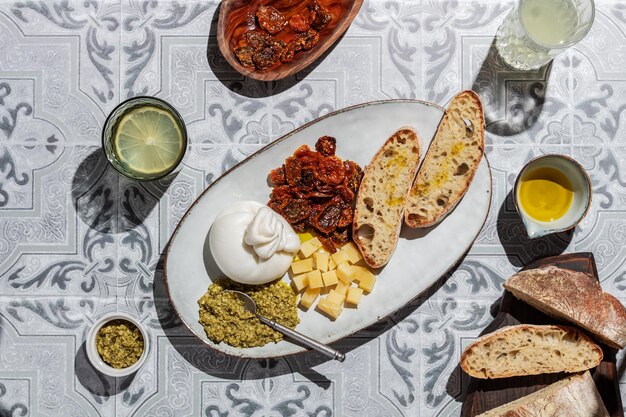 Foto burrata-käse auf einem teller mit brot, pesto-sauce und sonnengetrockneten tomaten