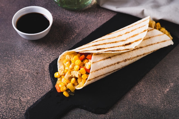 Foto burrito apetitoso em uma tortilha feita de milho de frango e pimentas em uma tábua de ardósia