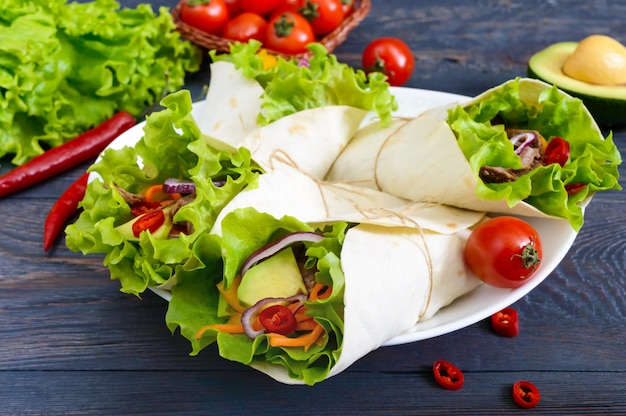 Burrito con carne picada, aguacate, verduras, pimiento picante en un plato sobre un fondo oscuro de la madera. Tortilla Rellena. Aperitivo tradicional mexicano.