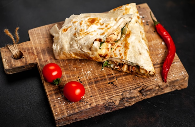 Burrito envolve com frango e legumes em uma tábua, contra um fundo de concreto, shawarma mexicano