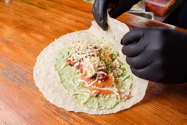 Foto burrito-herstellungsprozess. der küchenchef wickelt gefüllte pita auf einen holztisch. mexikanisches gericht.