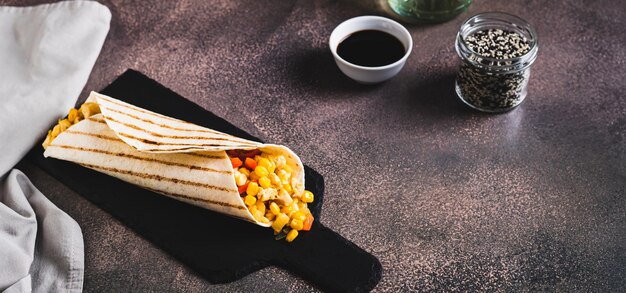 Foto burrito mexicano com frango de milho e pimentas em uma tortilha em um banner da web de tabuleiro de ardósia